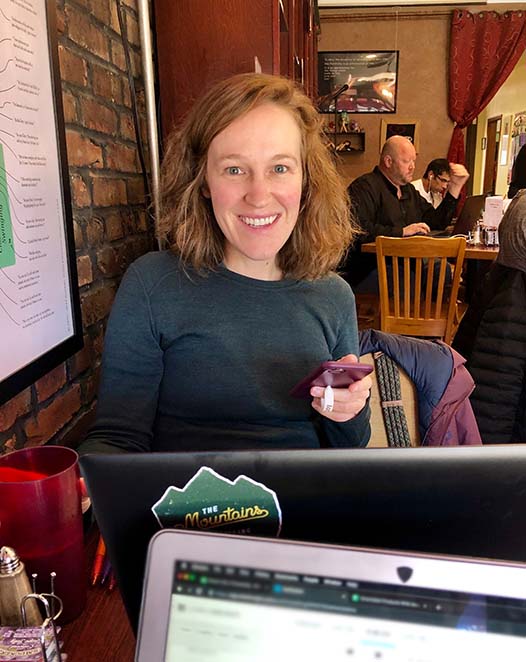 Christie Carbery sitting in front of a laptop holding a cell phone in a coffee shop